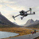 Квадрокоптер DJI Mavic 3 Enterprise летит над дорогой в горах рядом с людьми и автомобилем