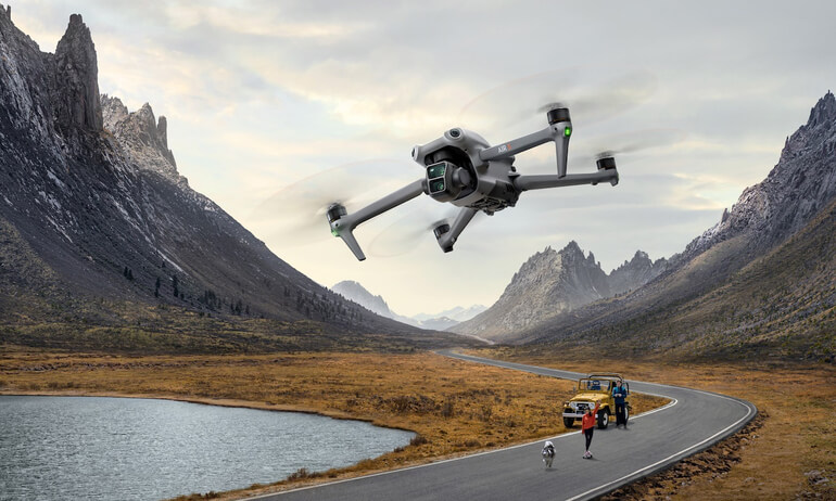 Квадрокоптер DJI Mavic 3 Enterprise летит над дорогой в горах рядом с людьми и автомобилем