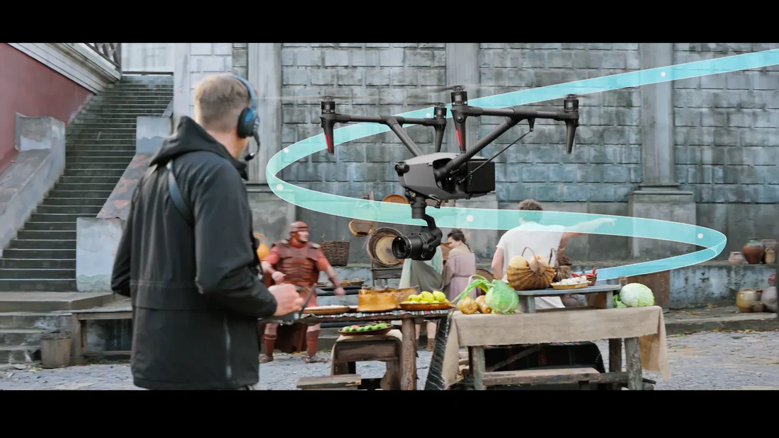 Профессиональный дрон DJI Inspire 3 летит над историческим рынком, снимая сцену с оператором на переднем плане, окружённой актёрами и реквизитом